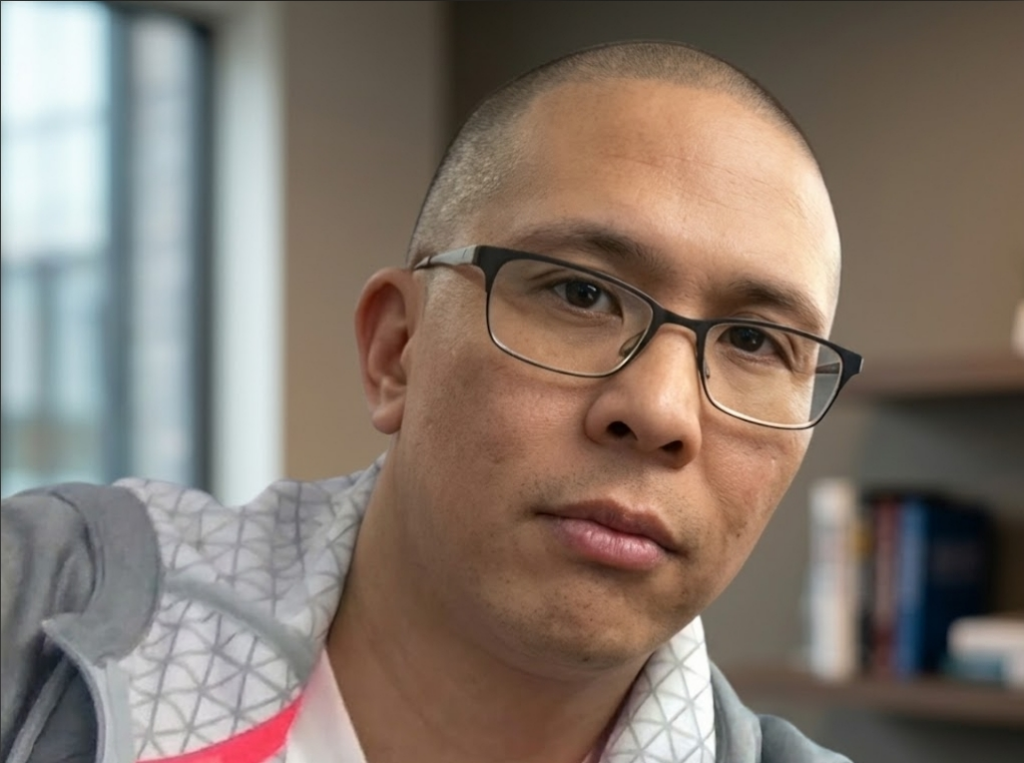 Profile photo of Eric Depusoy, also known as DJ E-Rok, who sits forward. He is a man with light tan complexion, a shaved head with glasses.